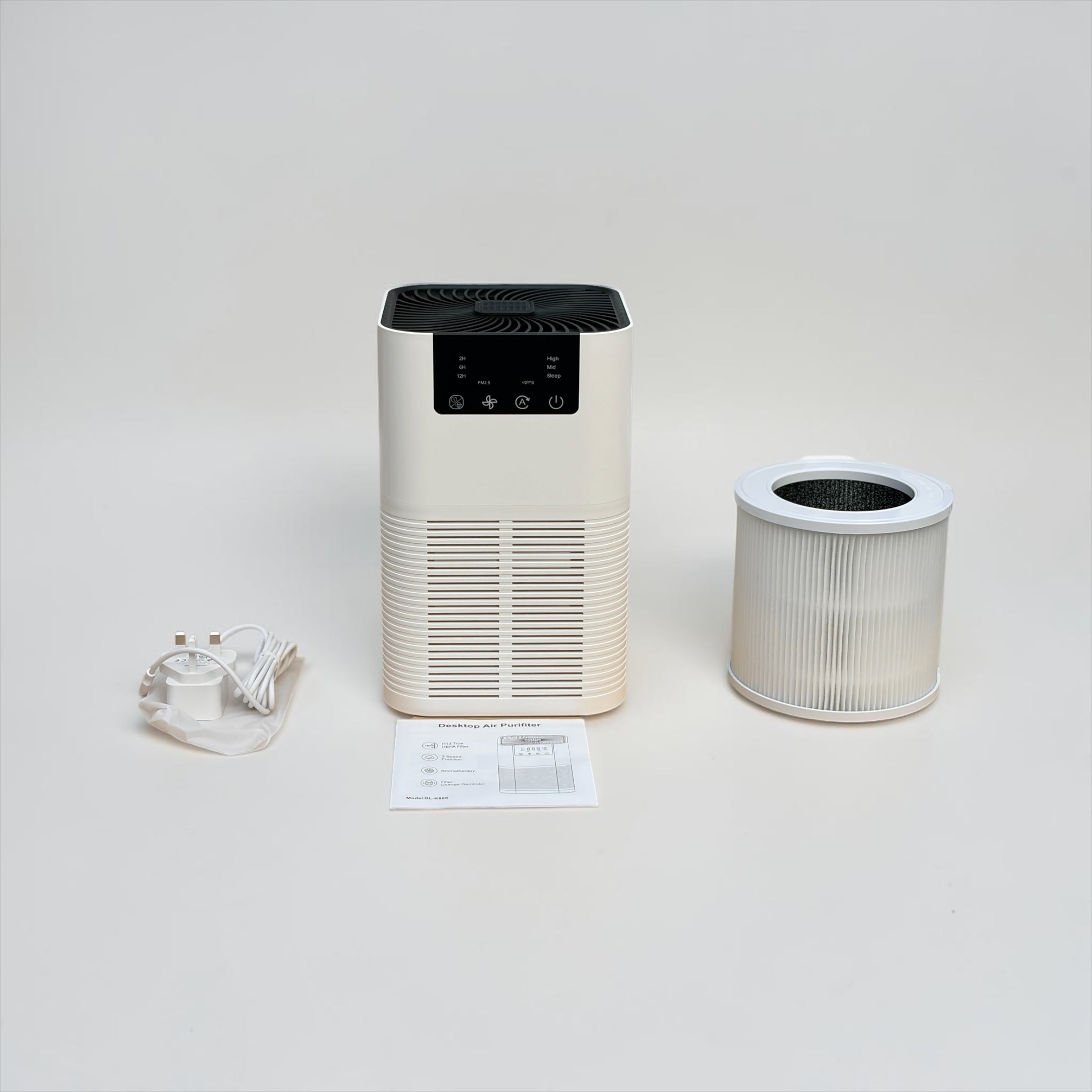 Full unboxing flat lay of the NuVibe™ Desktop Air Purifier set showing the main unit in cream white, a cylindrical 3-in-1 HEPA replacement filter with activated carbon layer, UK plug power adapter with cable, and printed instruction manual – everything included for immediate setup