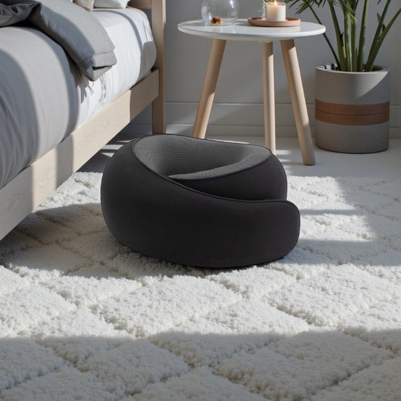 NuVibe™ ErgoNick Pillow in Pure Black beside a bed, ergonomic neck pillow designed for all-round neck comfort and relaxed home lounging.