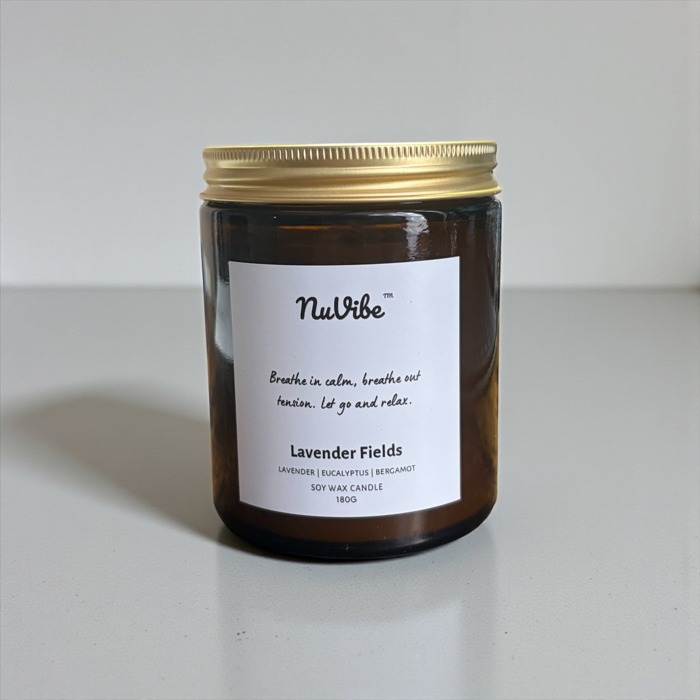 NuVibe lavender fields soy wax candle in amber glass jar with lit flame, surrounded by fresh lavender flowers, natural essential oil candle for relaxation and home fragrance
