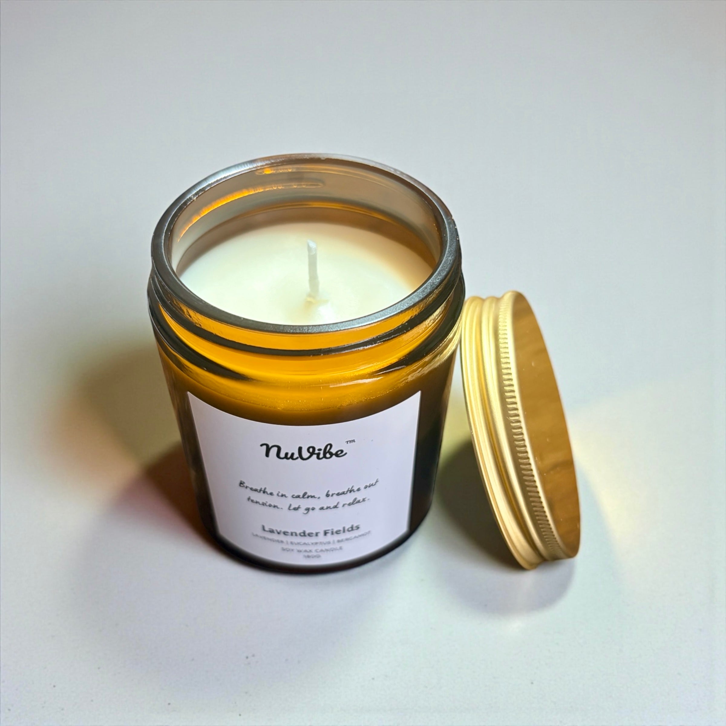 NuVibe lavender fields soy wax candle in open amber glass jar with lid off, showing smooth natural soy wax and cotton wick, essential oil home fragrance candle for relaxation.