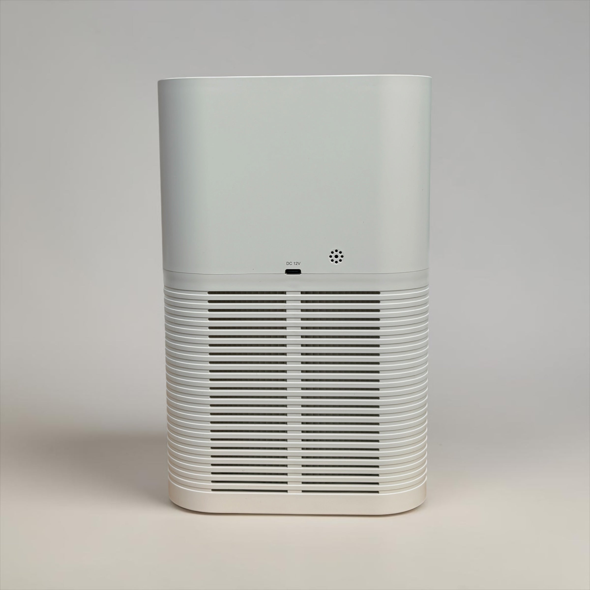 Rear view of the NuVibe™ Desktop Air Purifier in white, showcasing the DC 12V charging port, compact speaker grille, and horizontal air intake slats – a portable, quiet HEPA air purifier suitable for desks, bedrooms, and small room.