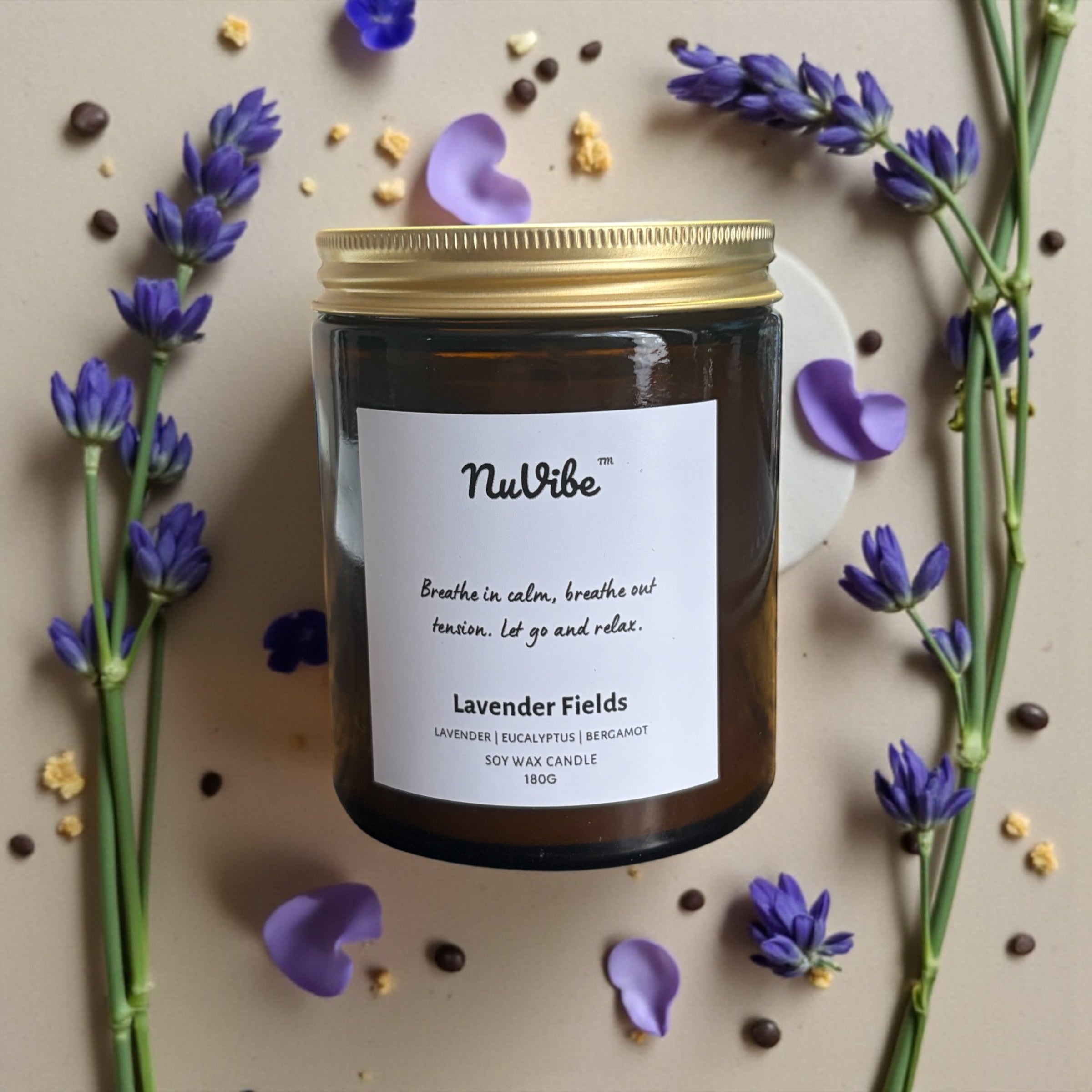 Bird’s eye view of NuVibe lavender fields soy wax candle in amber glass jar surrounded by fresh lavender flowers, natural essential oil home fragrance candle for relaxation