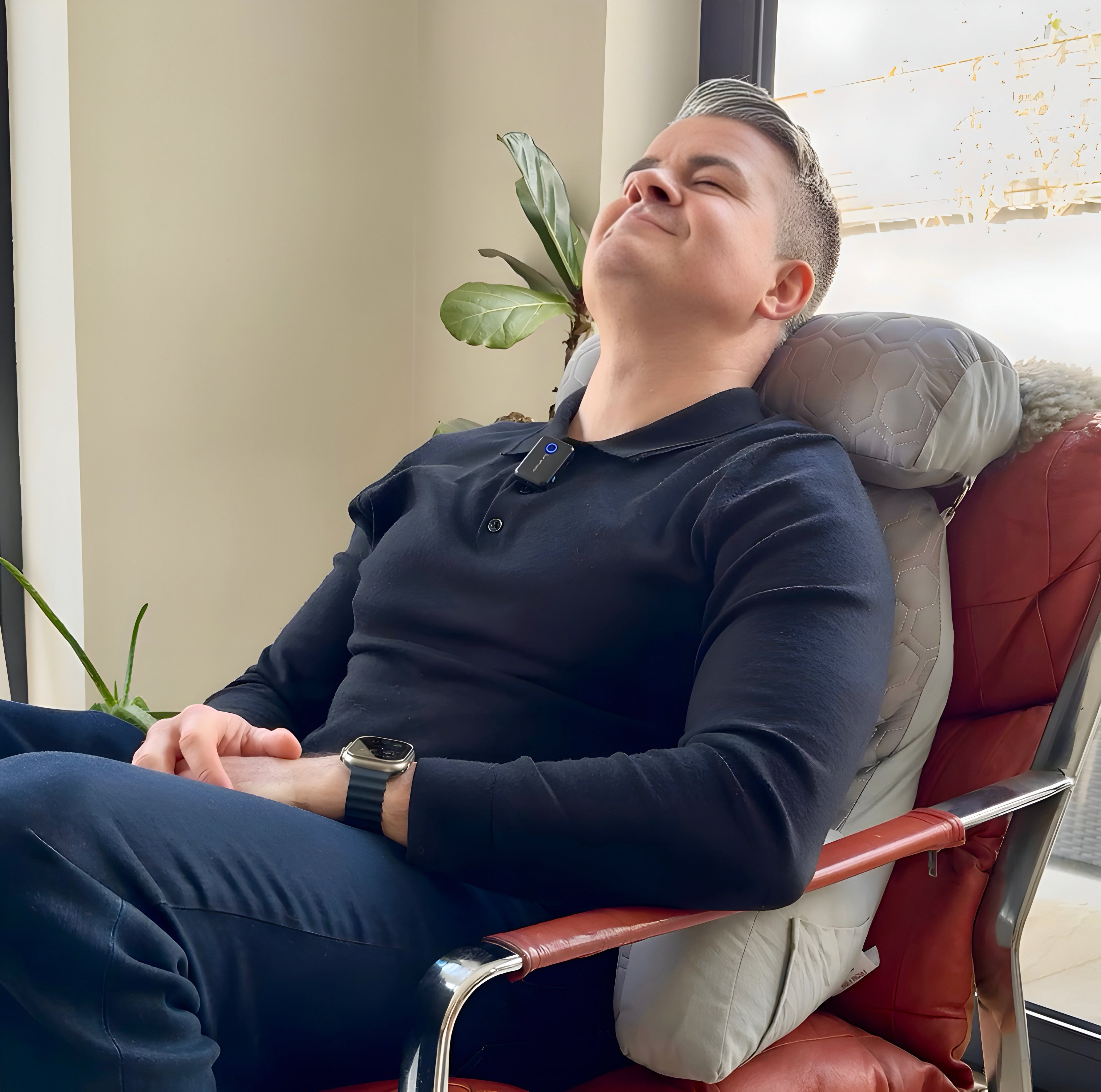 Man experiencing back pain finds relief using the NuVibe back support cushion on a living room sofa, ergonomic design for posture correction and daily comfort